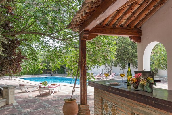 A poolside area with a pergola, lounge chairs, and a bar area with a vase of flowers.