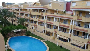 A hotel with a swimming pool surrounded by a well-maintained lawn and palm trees.