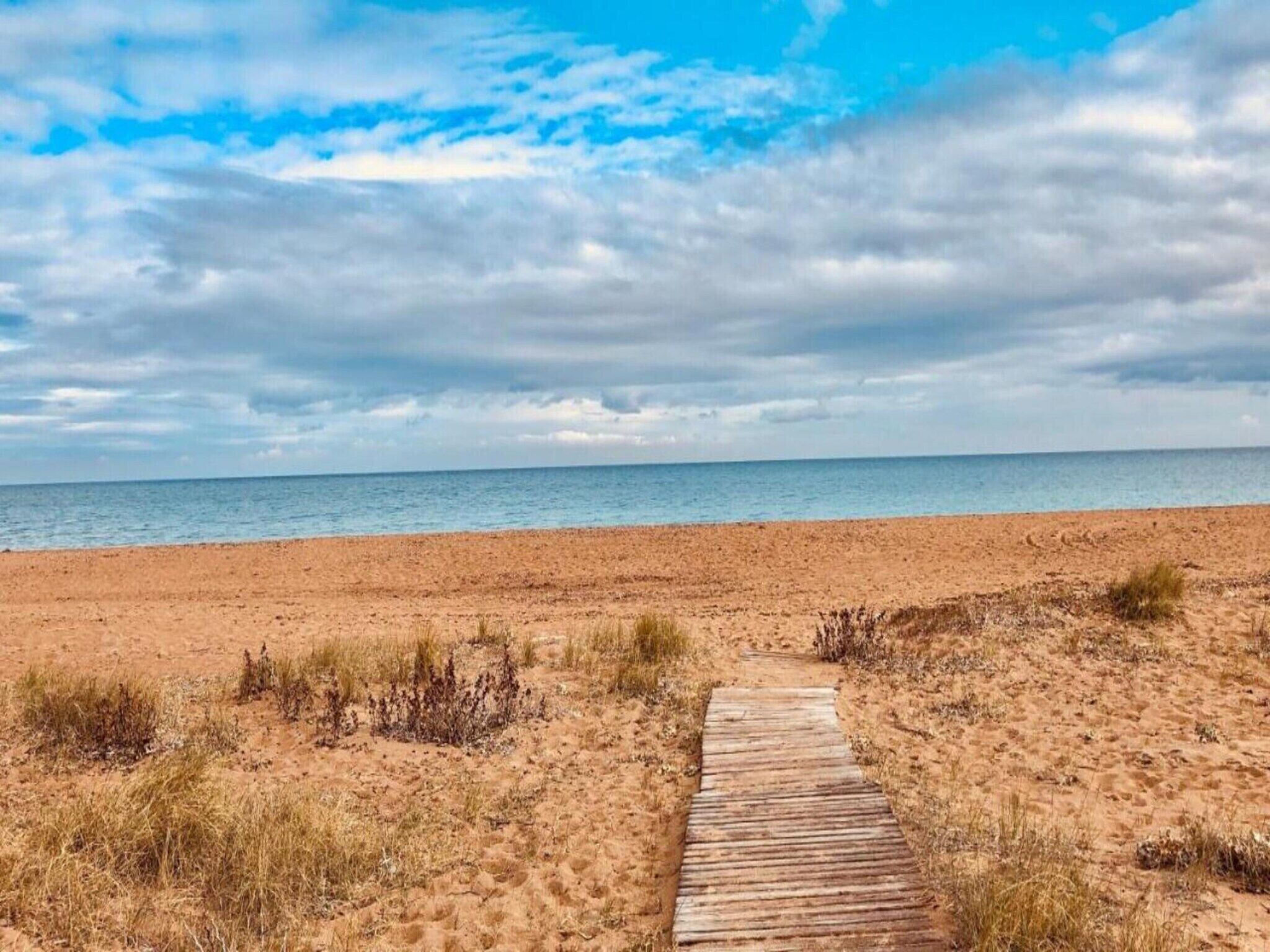 A sandy beach with a wooden pathway leading to the water.