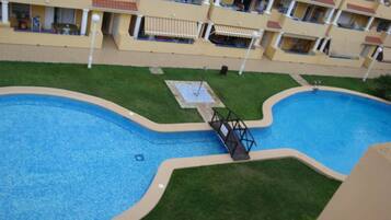 A swimming pool with a bridge, surrounded by a well-maintained lawn and a multi-story building with balconies.