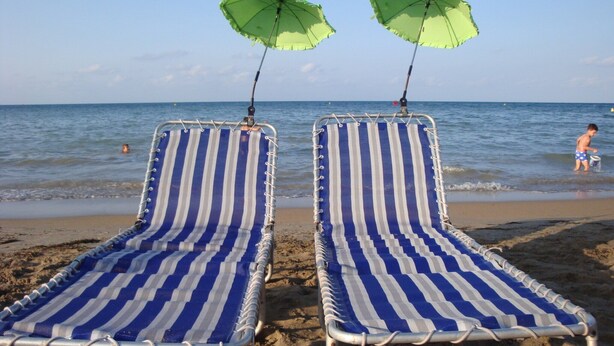 Two striped beach chairs with green umbrellas on a sandy beach by the sea.