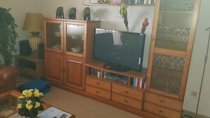 A living room with a television, wooden cabinets, a bookshelf, and a glass cabinet with decorative items.