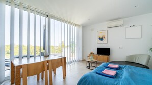 A hotel room with a large window, a bed with blue bedding, a wooden table, a TV, and a small table with a vase. - Modern Stay near Monte Solana (Pedreguer)