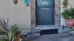 A building entrance with a dark metal door, a brick archway, and a small garden area with potted plants. - Panoramic cottage 100 mt from the main square view Taormina and Calabria (Castelmola)