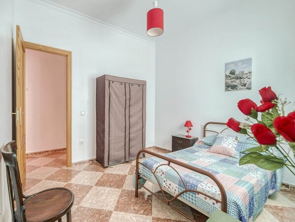 Een slaapkamer met een bed, een kledingkast, een stoel, een nachtkastje en een schilderij aan de muur.