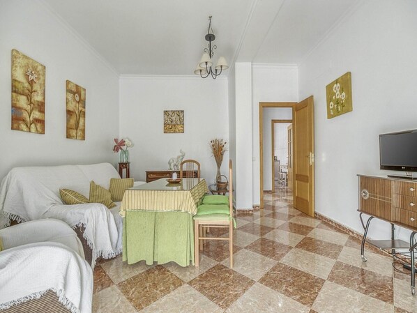 Una sala de estar con un sofá, una mesa de comedor con sillas, un televisor sobre un mueble de madera y obras de arte en las paredes.