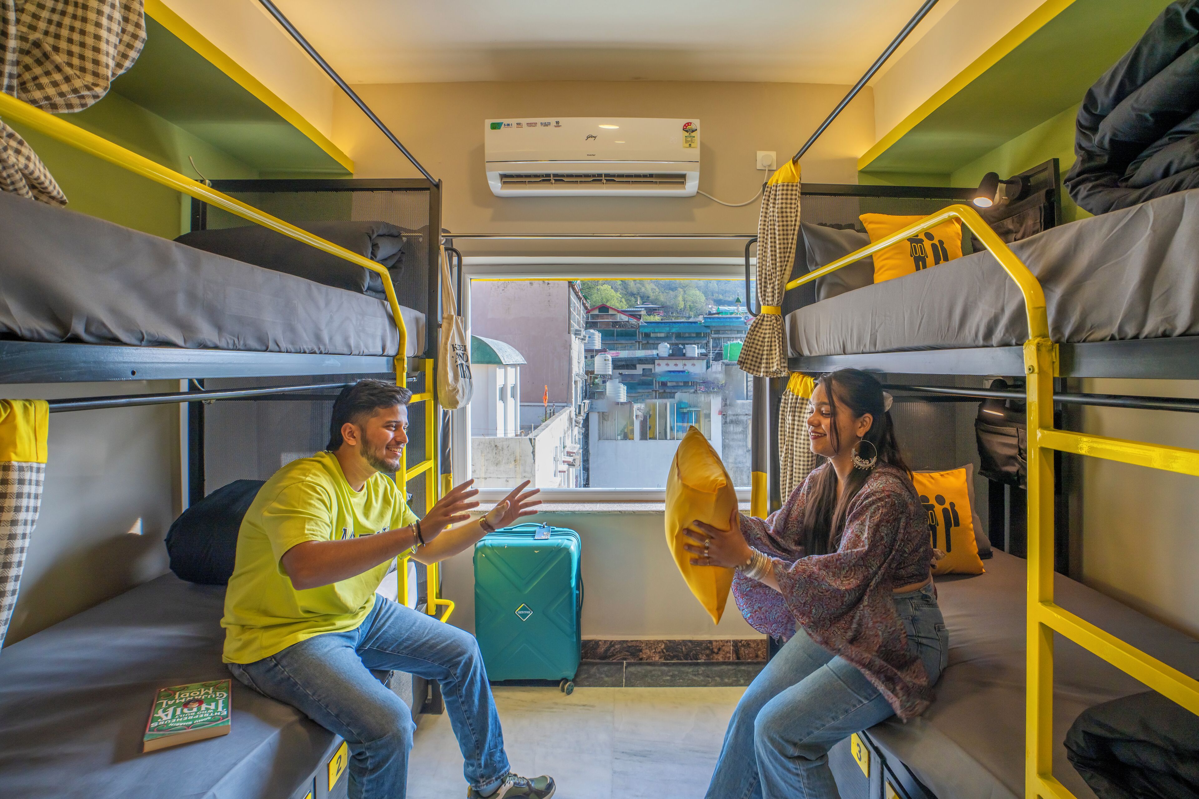 A train compartment with bunk beds, a suitcase, and a window with a view of buildings.