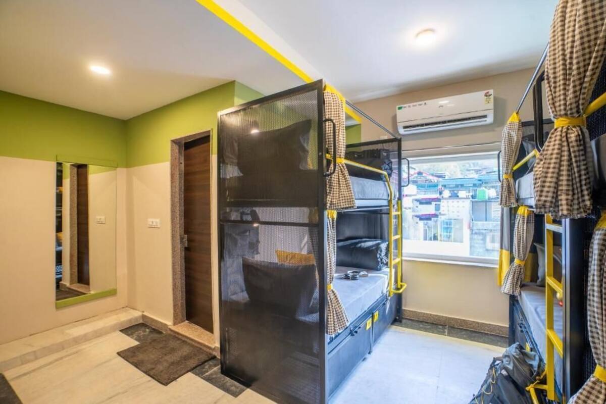 Une chambre d’hôtel compacte avec des lits superposés, une fenêtre donnant sur la ville et une porte menant à une autre chambre.