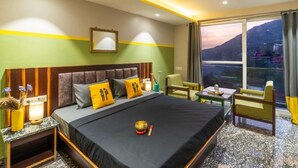 A hotel room with a bed, a nightstand, a table, a chair, and a view of a mountain. - The Hosteller Rishikesh, Ganges (RISHIKESH)