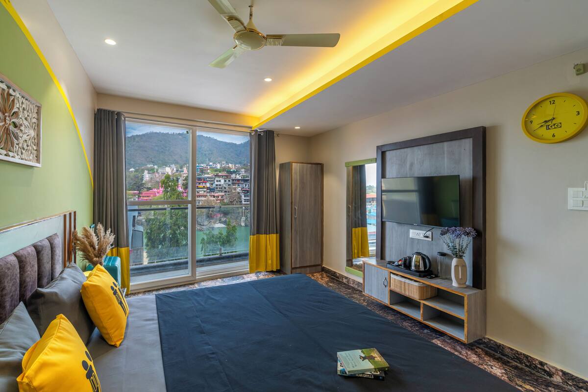 Une chambre d’hôtel moderne dotée d’un grand lit, d’un téléviseur à écran plat, d’un ventilateur de plafond et offrant une vue sur le paysage urbain par la fenêtre.