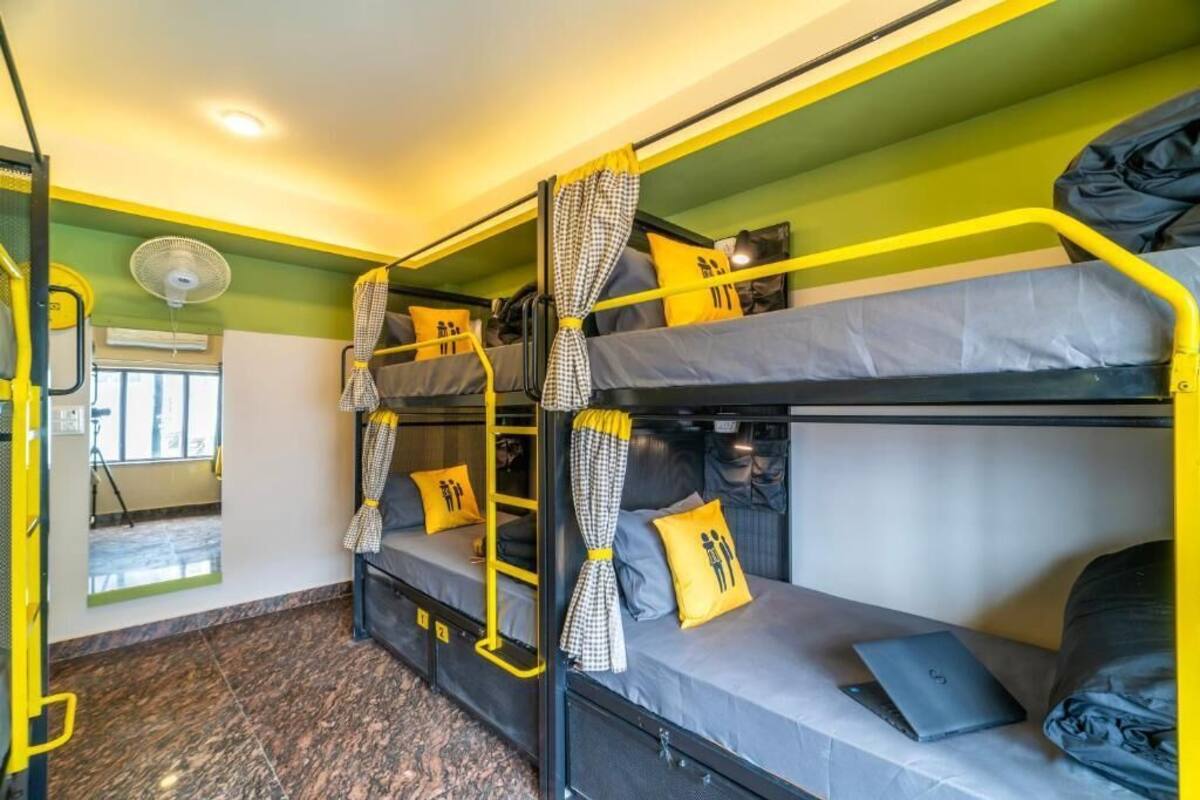 Une chambre avec un lit superposé, des barreaux jaunes, une literie grise et un ventilateur.