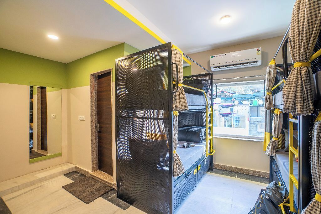 A room with bunk beds, a window with a city view, an air conditioning unit, and a mirror.