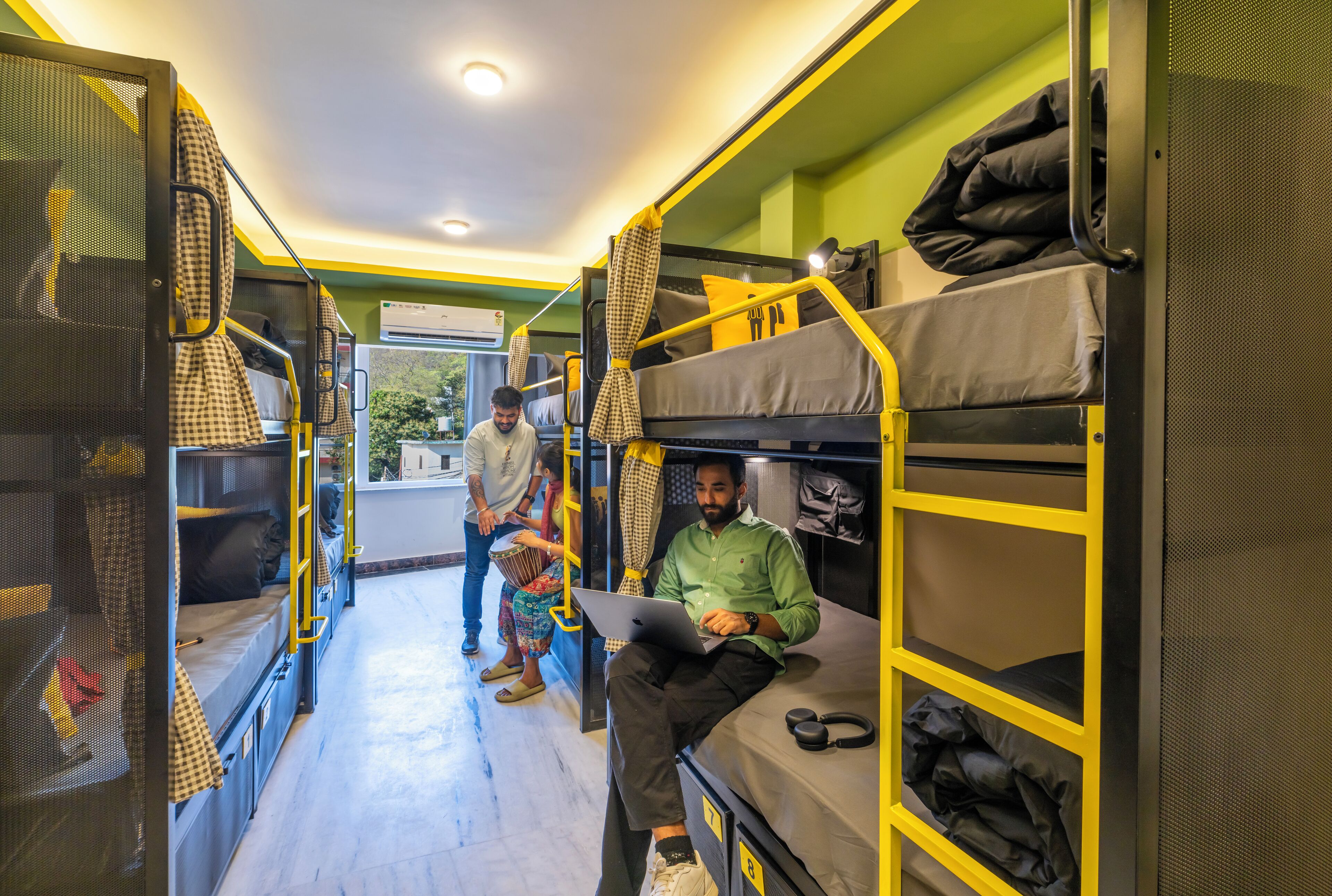 A hostel room with bunk beds, a laptop on one bed, and a person sitting on the lower bunk.