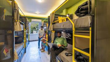 A hostel room with bunk beds, a laptop on one bed, and a person sitting on the lower bunk.