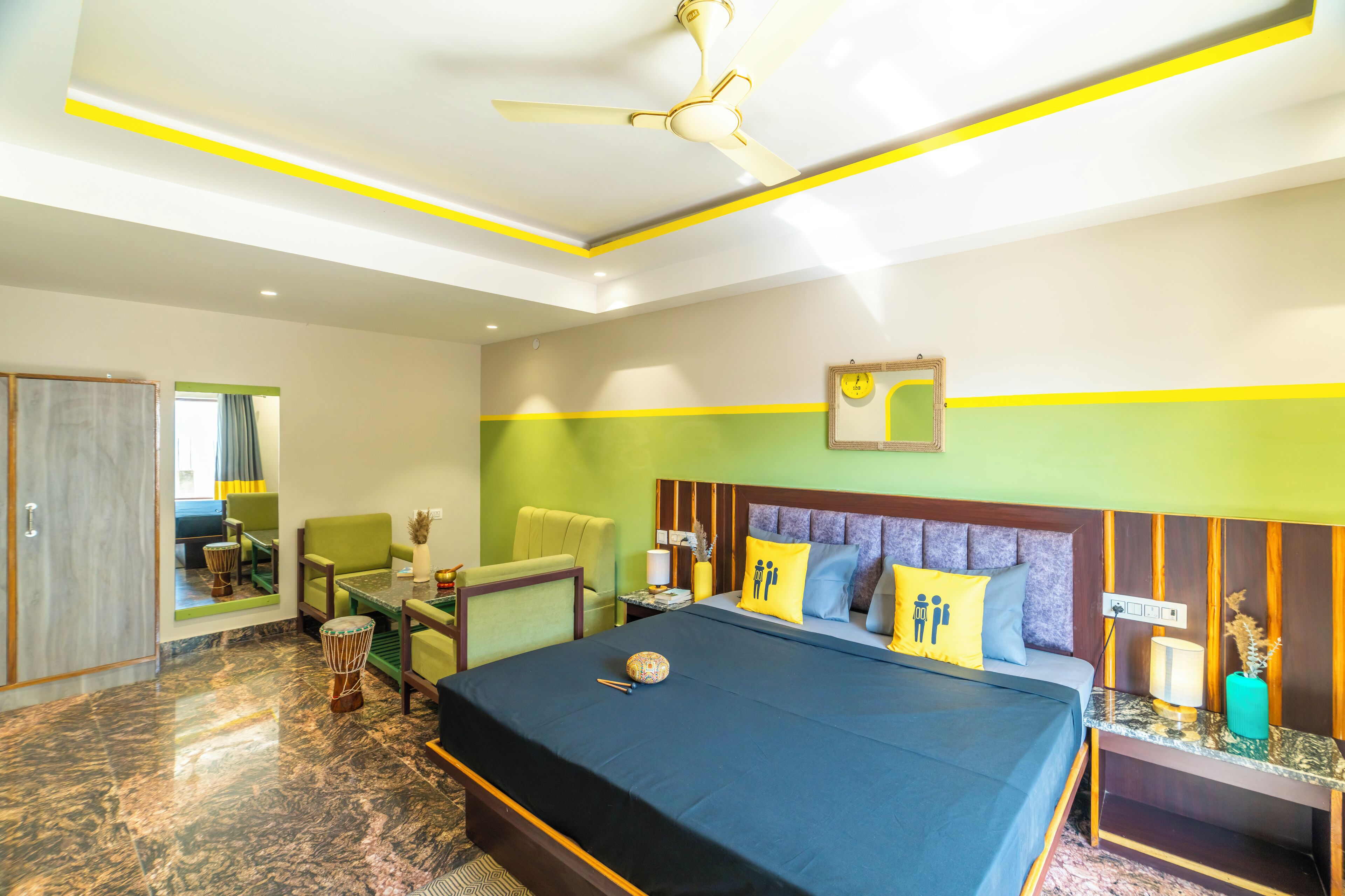 A hotel room with a bed, green and yellow walls, a ceiling fan, and a small table with chairs.