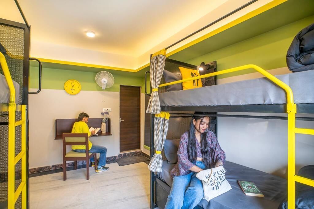 Habitación con literas, escritorio, silla, ventilador y un reloj en la pared.