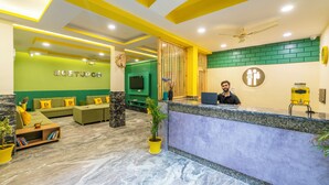 A reception area with a marble floor, green and yellow walls, a reception desk, and a seating area with cushions. - The Hosteller Rishikesh, Ganges (RISHIKESH)