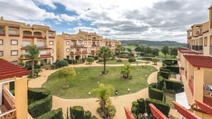 A courtyard with a central lawn, surrounded by multi-story buildings with balconies and a view of distant hills.