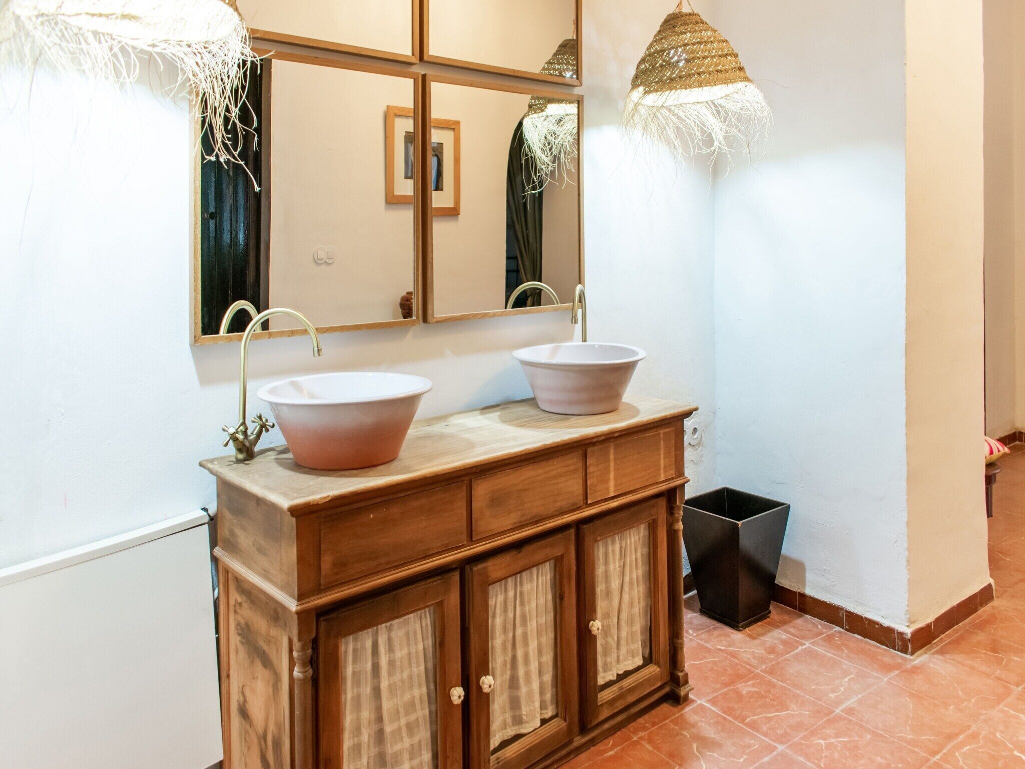 Un baño con tocador de madera, dos lavamanos, un espejo y dos luces colgantes.