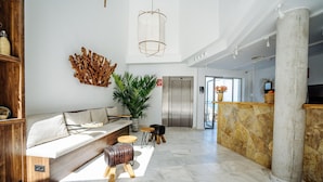 A spacious lobby with a modern sofa, a large potted plant, a wooden bench, and a stone reception desk.