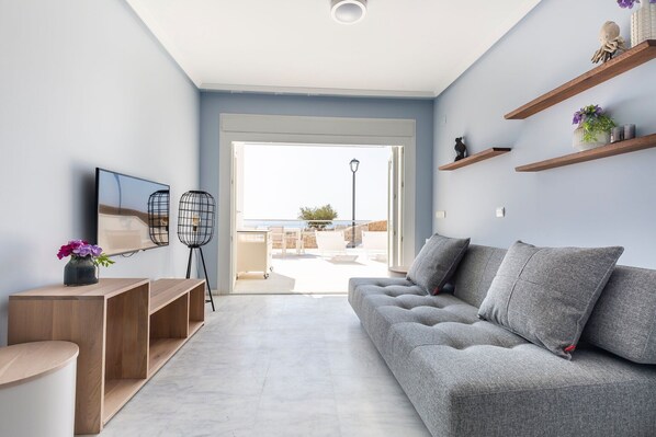 A modern living room with a grey sofa, wooden shelves, and a large window.