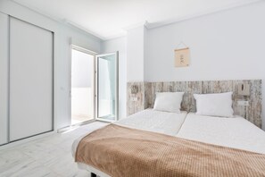 A bedroom with a bed, a wooden headboard, a wall-mounted light, and a sliding glass door leading to a balcony.