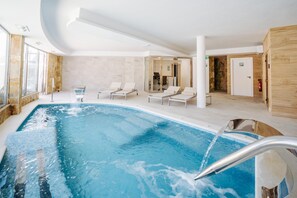 An indoor swimming pool with lounge chairs and a glass door leading to a shower area.