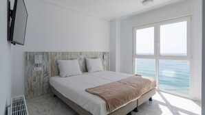 Un dormitorio con cama, televisión montada en la pared y un ventanal con vista al mar.