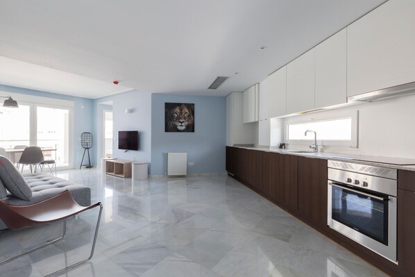 A modern kitchen with a built-in oven and a dining area with a grey sofa and a chair.