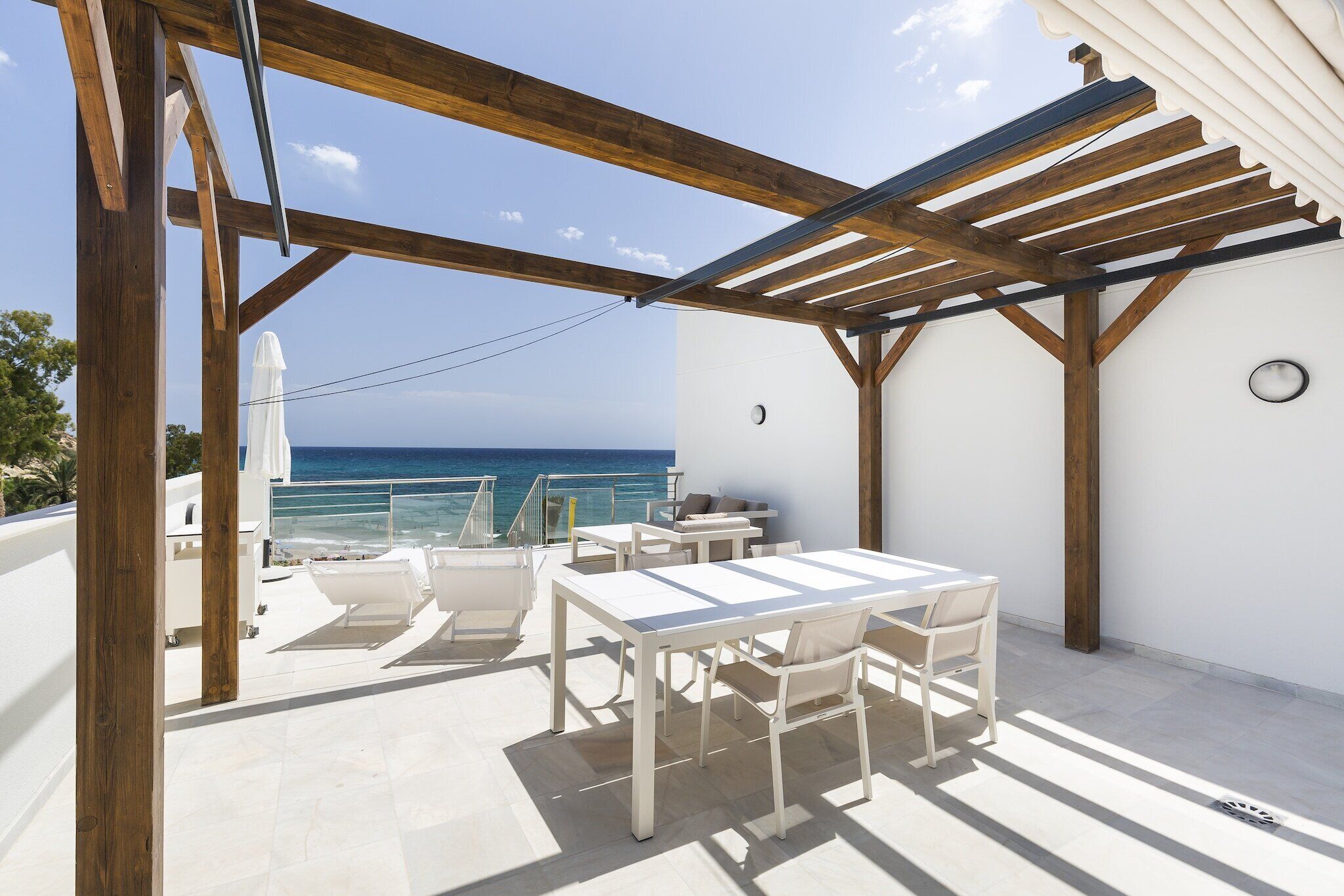 Une terrasse dotée d’une pergola en bois, de mobilier blanc et offrant une vue sur la mer.
