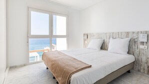 A bedroom with a large bed, a wooden headboard, and a view of the sea through a large window.