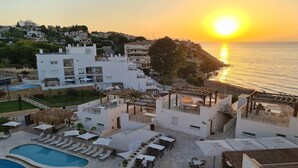 A resort with a pool, outdoor seating, and a view of the sunset over the sea.