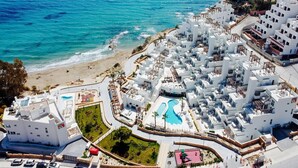 A coastal resort with white buildings, a beach, and a swimming pool.