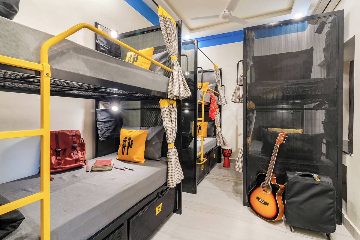 Une chambre avec un lit superposé, un sac rouge, une guitare et une valise.