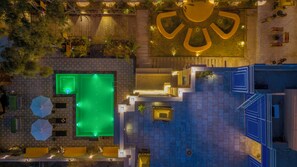 Vista aerea di un hotel con piscina, area salotto esterna e un grande logo illuminato.