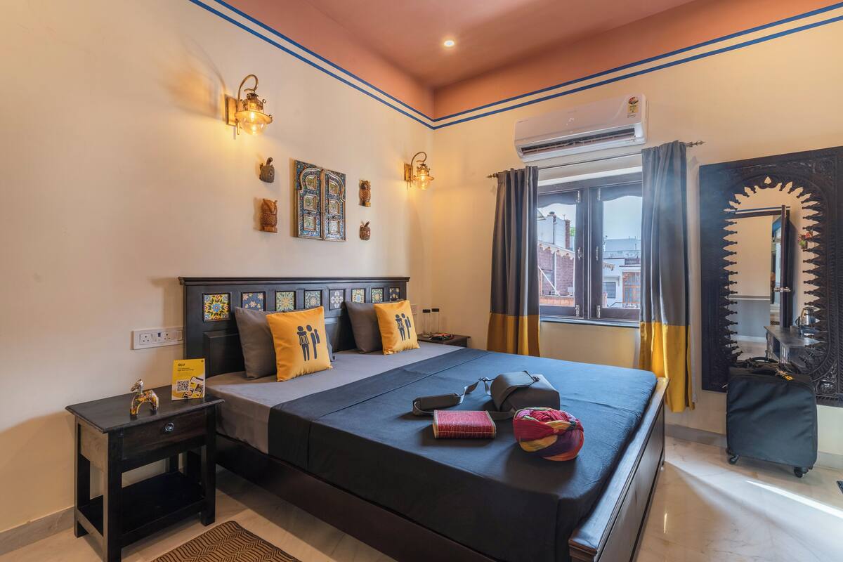 Une chambre d’hôtel avec un grand lit, des tables de chevet, des lampes fixées au mur, une fenêtre avec des rideaux et un appareil de climatisation.
