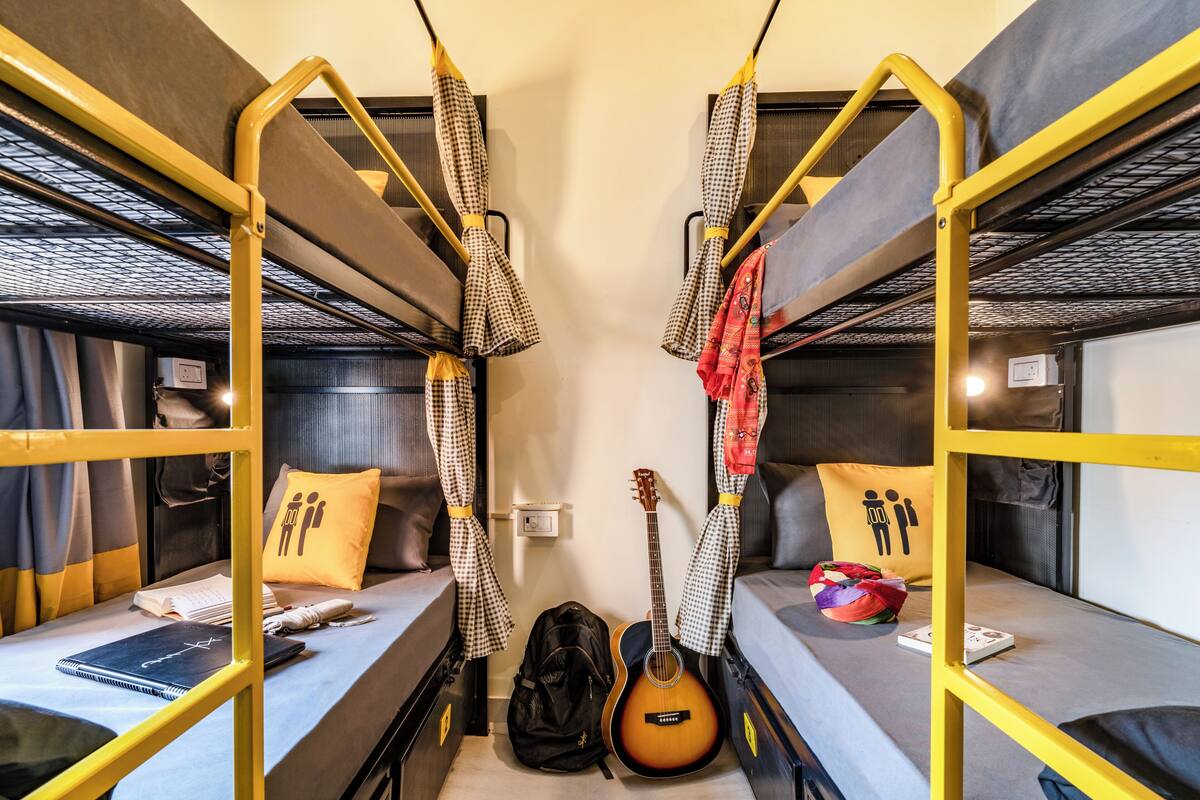 Une chambre avec un lit superposé, sur lequel on trouve une guitare, un sac à dos et un livre.