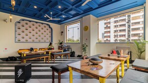 Un intérieur moderne avec un plafond bleu, des tables en bois et des bancs. Une grande fenêtre offre une vue sur l’extérieur.