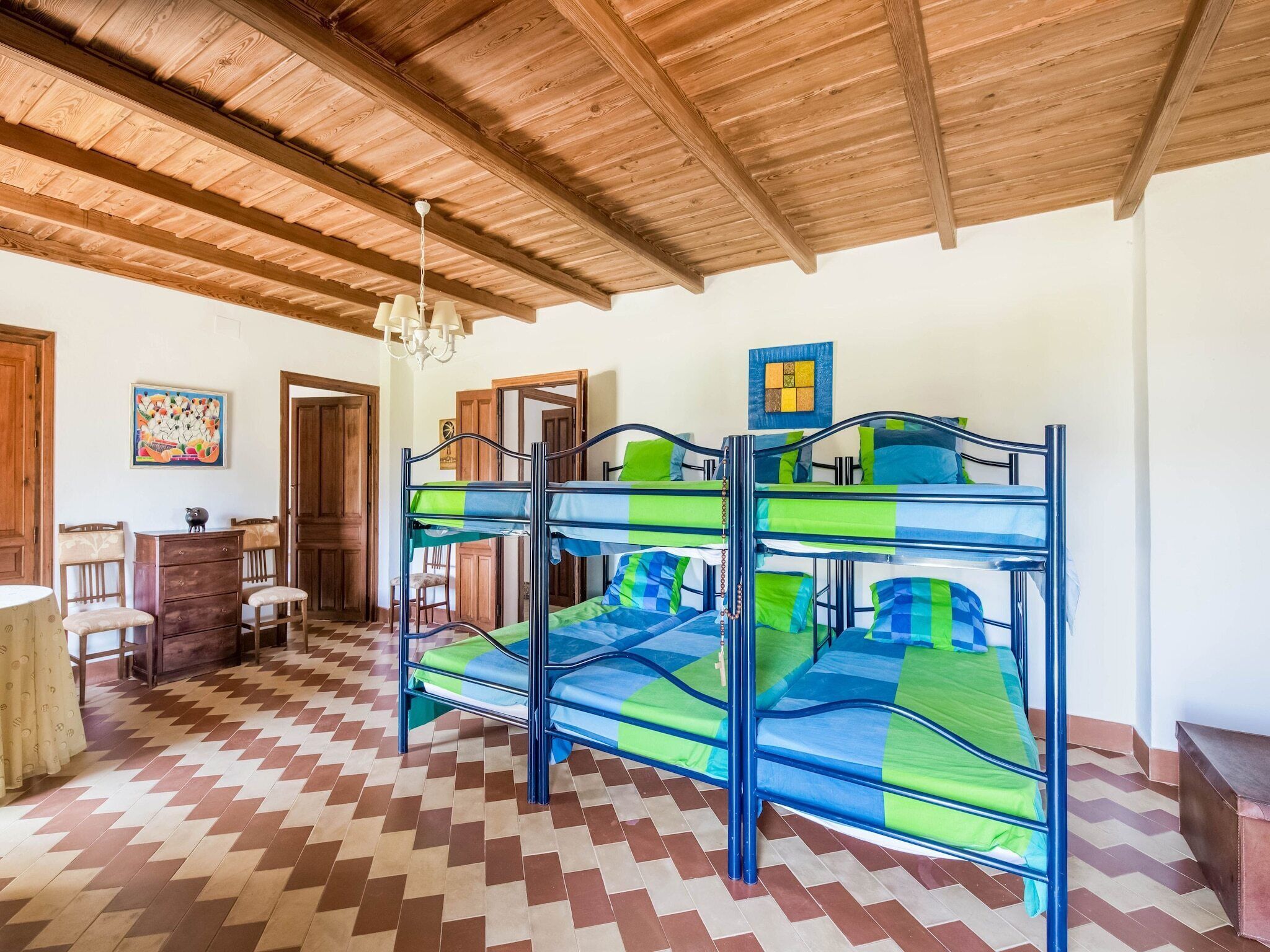 Una habitación con techo de madera, una litera con ropa de cama azul y verde, un aparador de madera y un suelo con estampado.