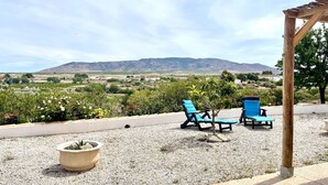 A patio with two blue lounge chairs, a small potted plant, and a pergola overlooking a mountainous landscape. - Cave House in Cúllar near Tabernas Desert (Cúllar)