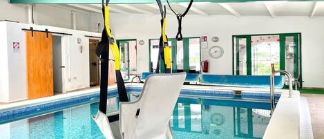 Una piscina interior con una silla de salvavidas, una puerta de madera y un ventanal con marco verde.