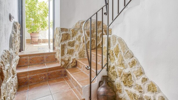 A staircase with stone walls and metal railings, leading to a door with a view of greenery outside. - Villa in Carcabuey near Sierras Subbeticas Park (Carcabuey)