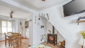 A cozy living room with a fireplace, a dining area with a wooden table and chairs, and a television mounted on the wall. - Villa in Carcabuey near Sierras Subbeticas Park (Carcabuey)
