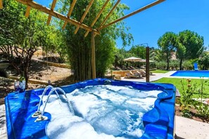 A hot tub with a wooden pergola overhead, surrounded by greenery and a pool in the background. - Holiday home in Carcabuey with private pool (Carcabuey)