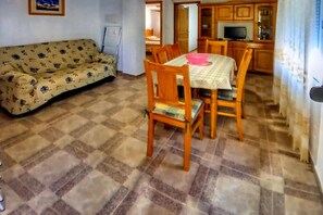 A living room with a sofa, dining table with chairs, and a kitchen area with cabinets and a television.