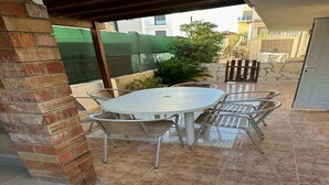 A covered patio area with a round table and four chairs, surrounded by a brick wall and a green fence. - Apartment near Beach with Serene Garden (Valencia)