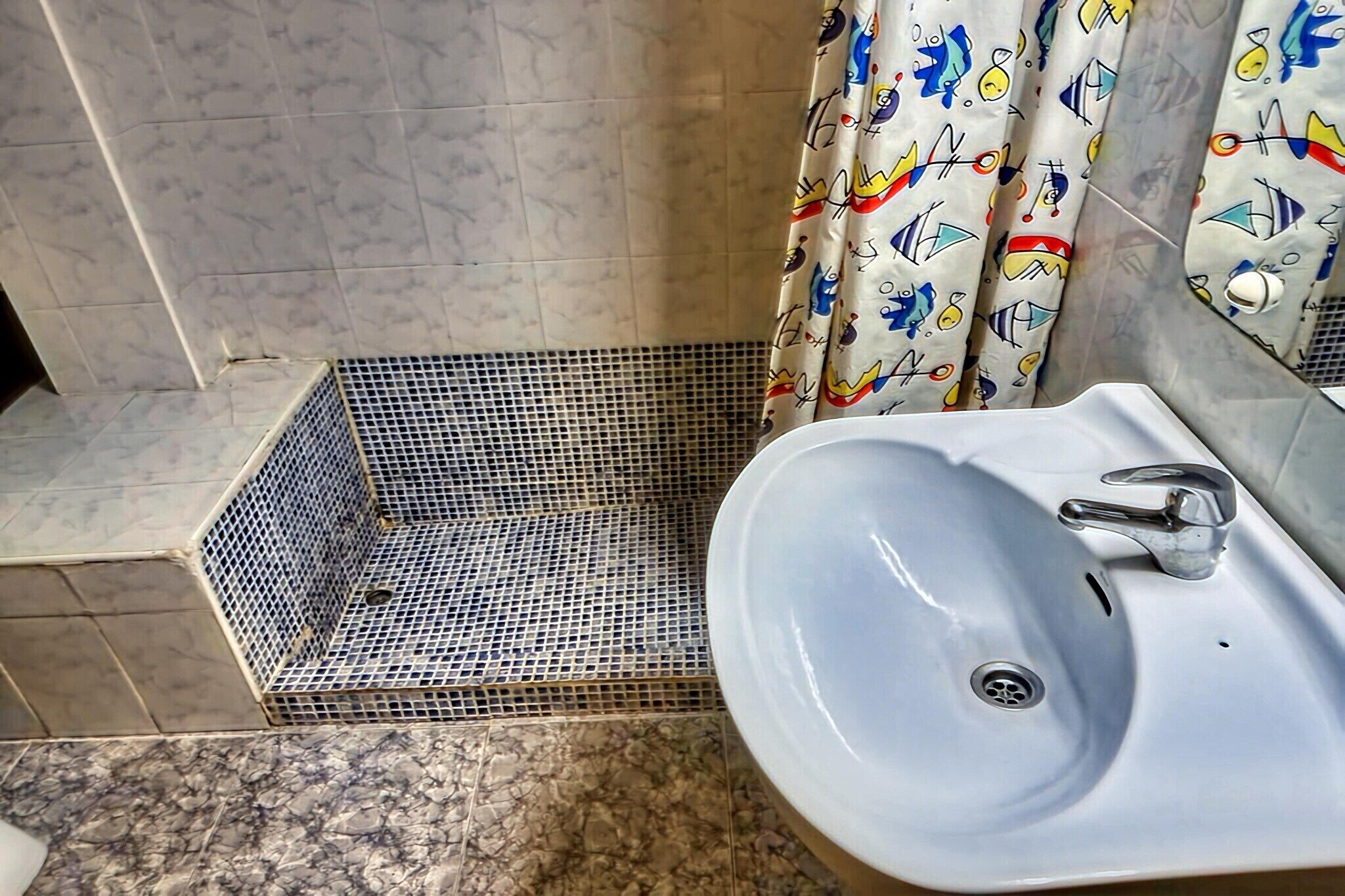A bathroom with a white sink, a shower with a tiled floor, and a shower curtain with a colorful pattern.