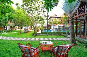 Relax in the serene garden, surrounded by lush trees and a tranquil seating area with wicker furniture.