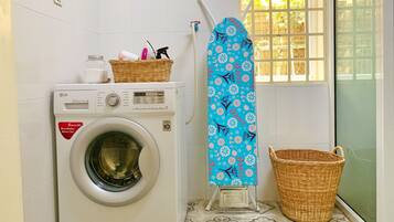 A laundry area with a washing machine, an ironing board, and a basket.