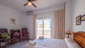 A hotel room with a bed, two wooden chairs, a small table, a ceiling fan, and a view of the city through the balcony doors. - Penthouse in Denia with Private Terrace (Denia)